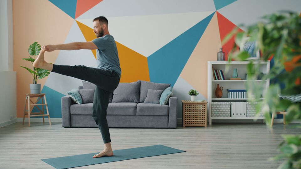 Man doing a calm standing stretch on a yoga mat in a bright living room