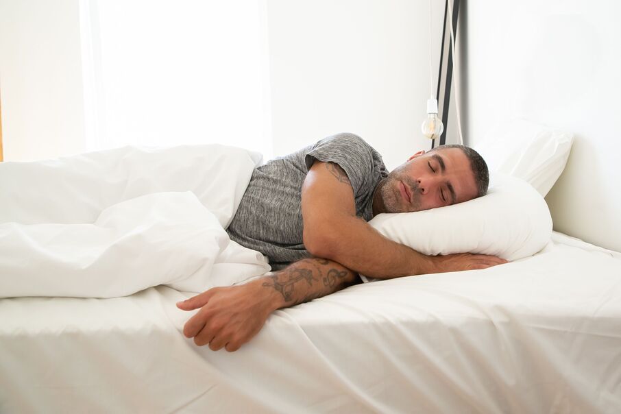 Man sleeping on his side under a white duvet, head resting on a soft pillow