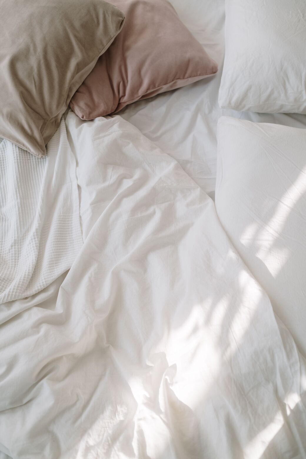 Soft white bed linen and rumpled pillows in gentle daylight